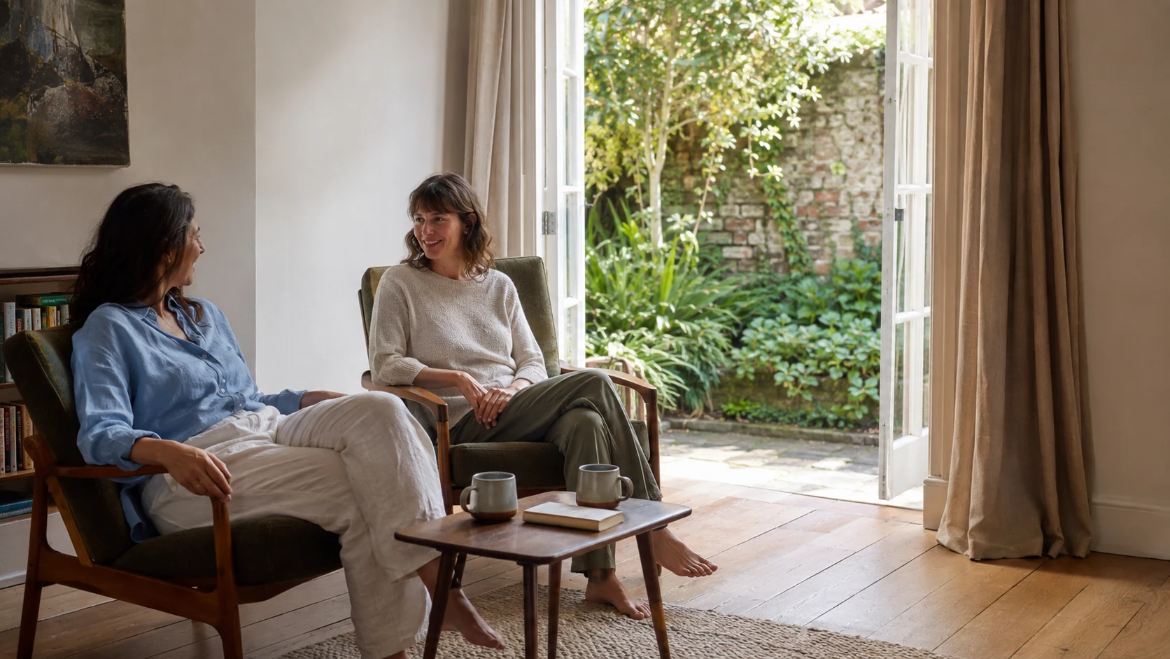 Two friends enjoying coffee beside open garden doors.